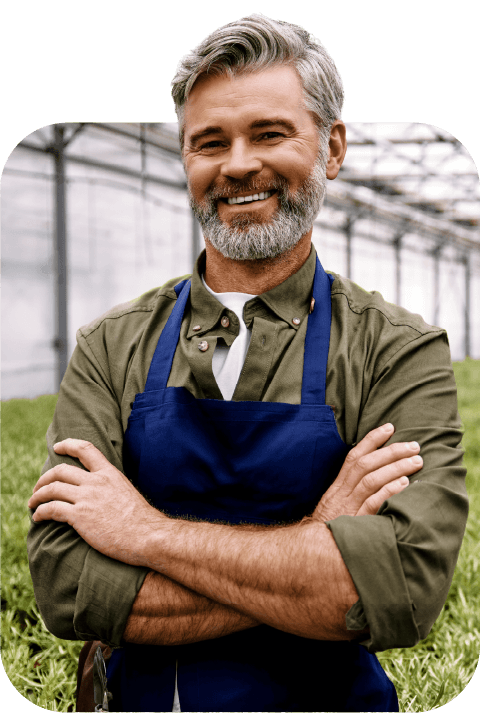 Produtor sorrindo, de braços cruzados, em uma estufa
